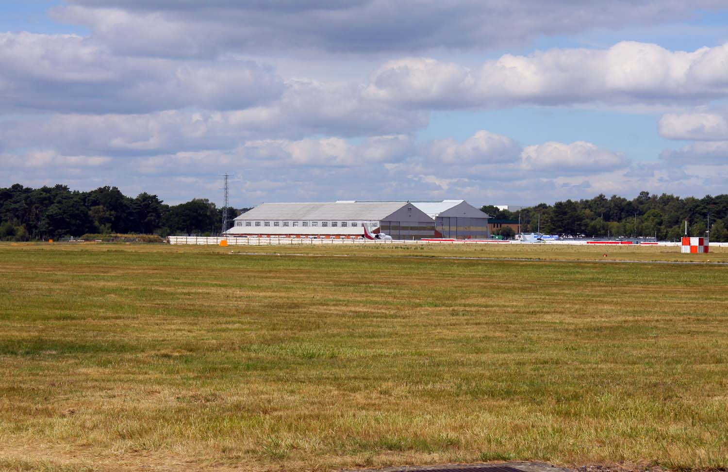 Real photograph across Farnborough Airfield in Hampshire, showing aircraft hangars, business jets on the apron and the wider airfield setting.