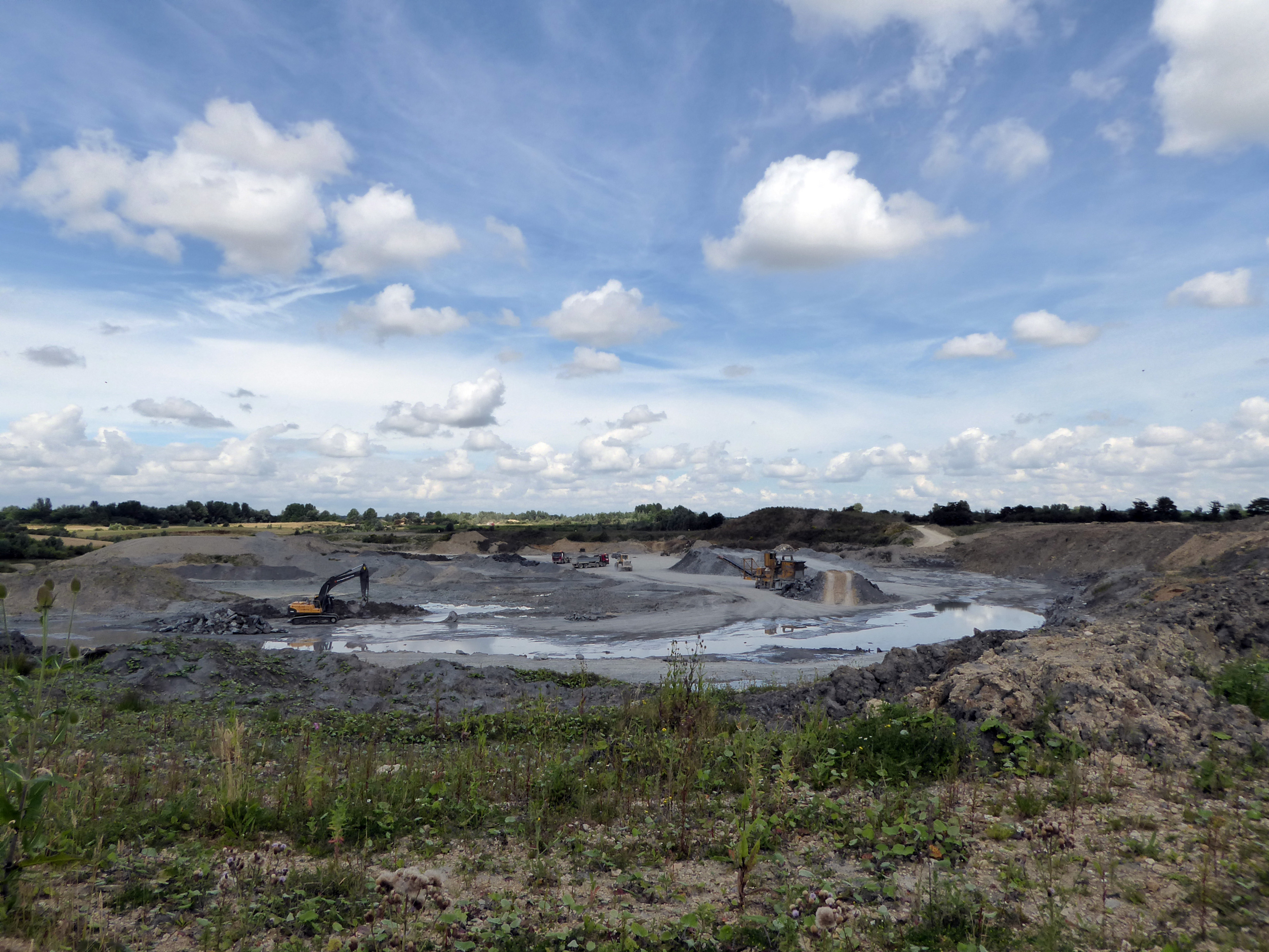Real photograph of Hills Quarry at Shorncote, Gloucestershire, showing an excavator, trucks, stockpiles and processing plant.