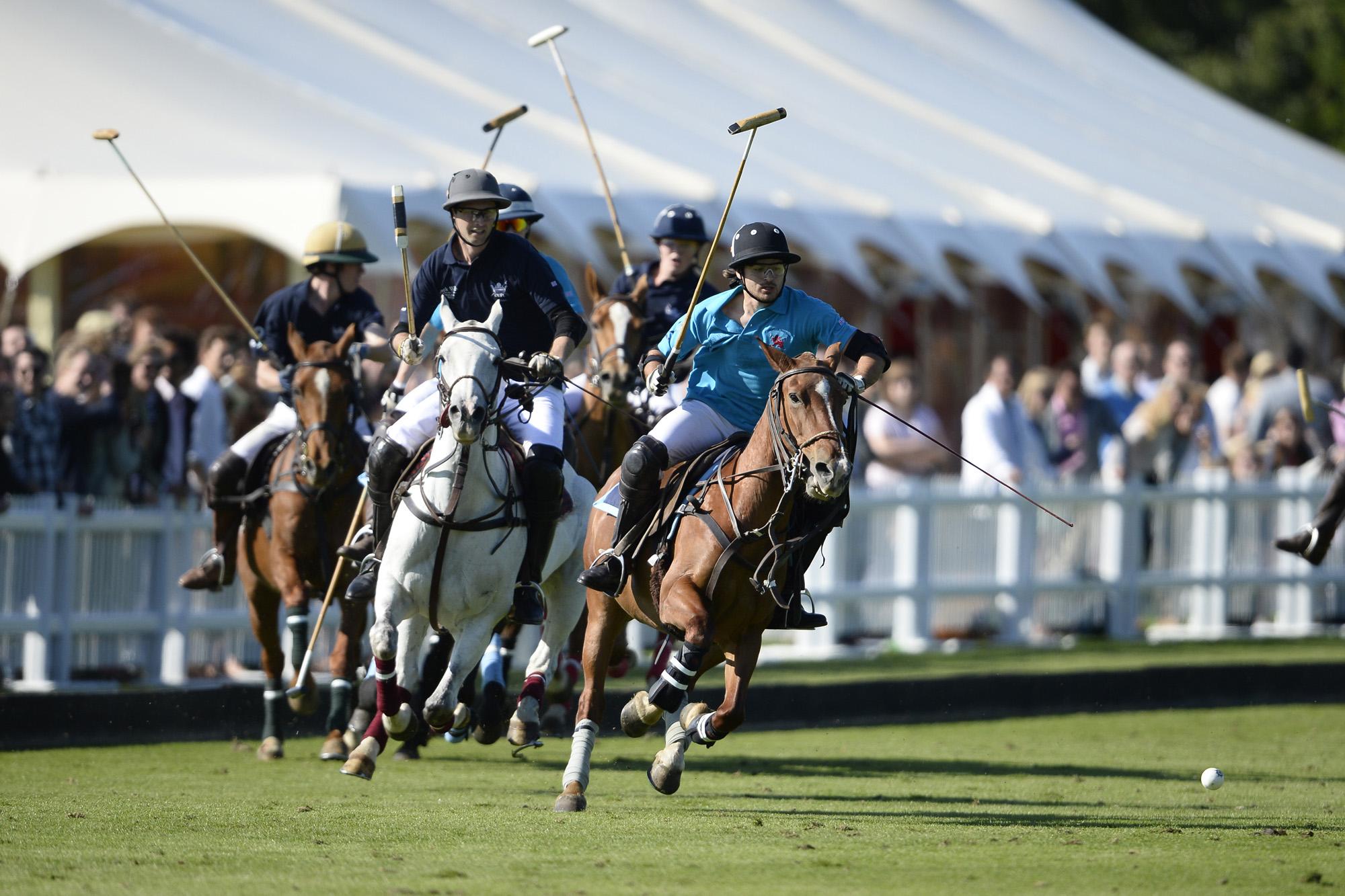 Real photograph of Oxford and Cambridge polo players and horses contesting the ball during Varsity Polo in 2013, with spectators and a marquee behind.