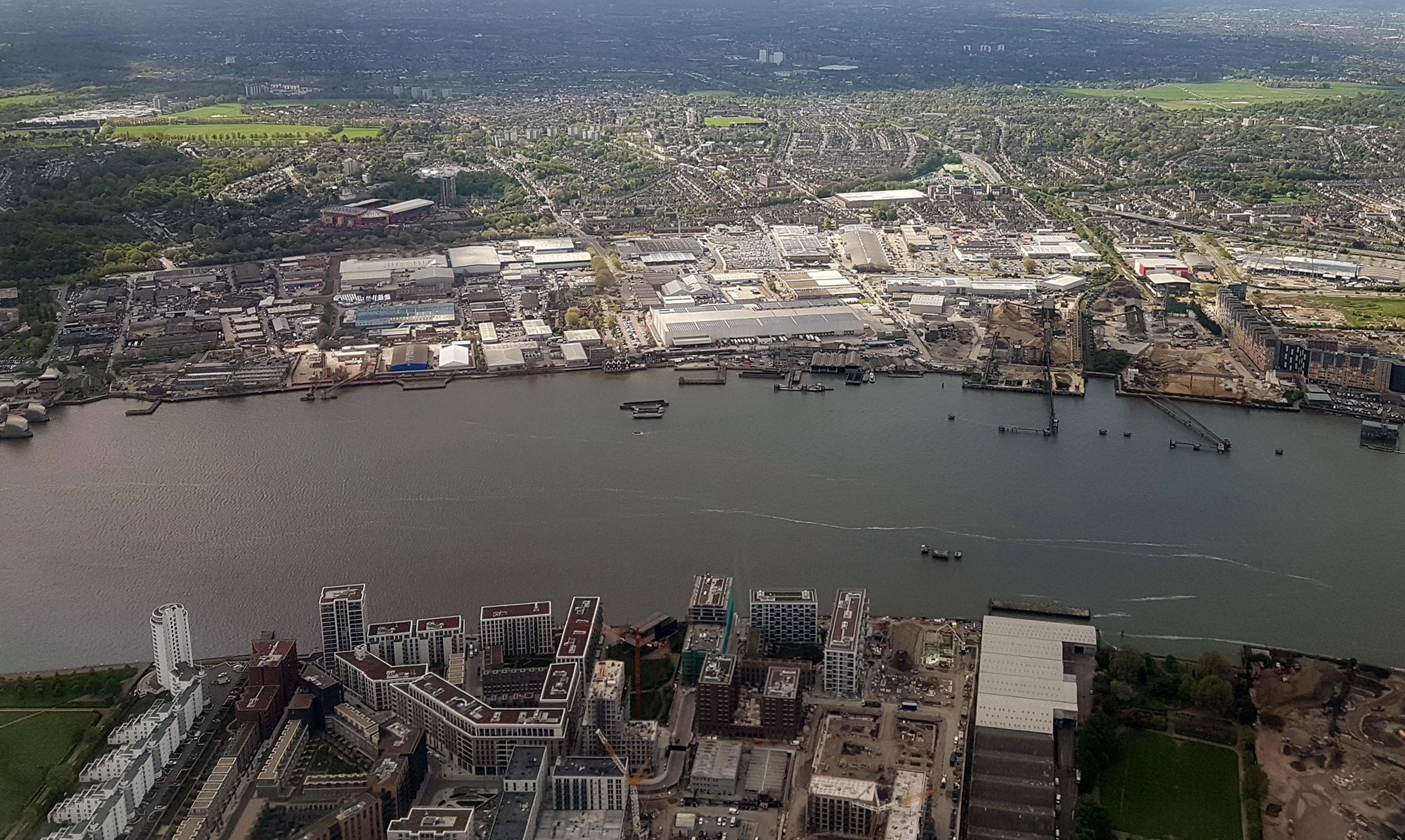 Real aerial reference photograph of Royal Wharf, the River Thames and Charlton Riverside in London, showing commercial buildings, industry and urban development.