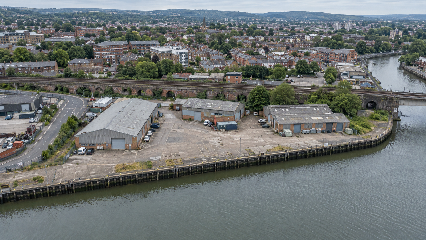 Illustrative drone view of an underused British waterside industrial asset, with three warehouses, empty hardstanding, quay, road and rail infrastructure.